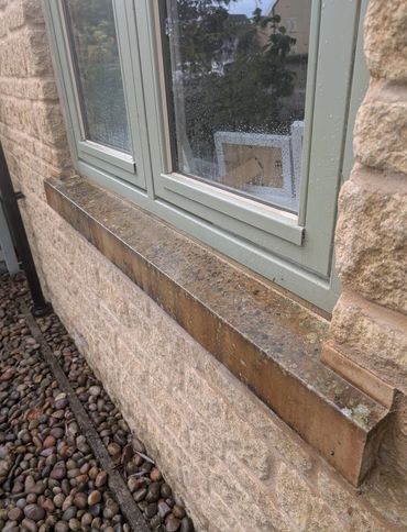 Rain droplets on a window with a stone wall and pebble ground outside.