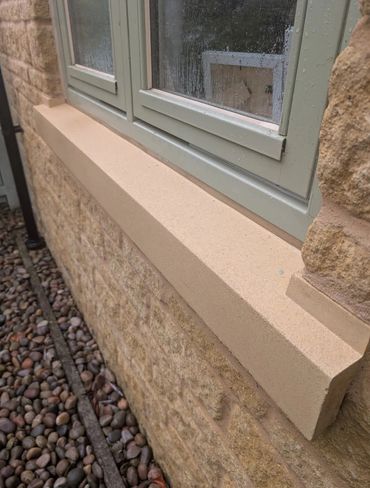 A close-up of a beige window sill on a stone wall with raindrops on the window.