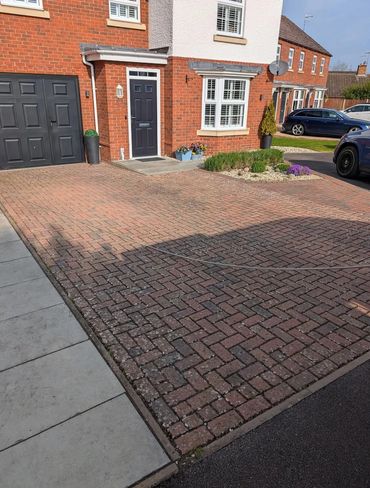Brick driveway leading to a black front door and garage of a red brick house.