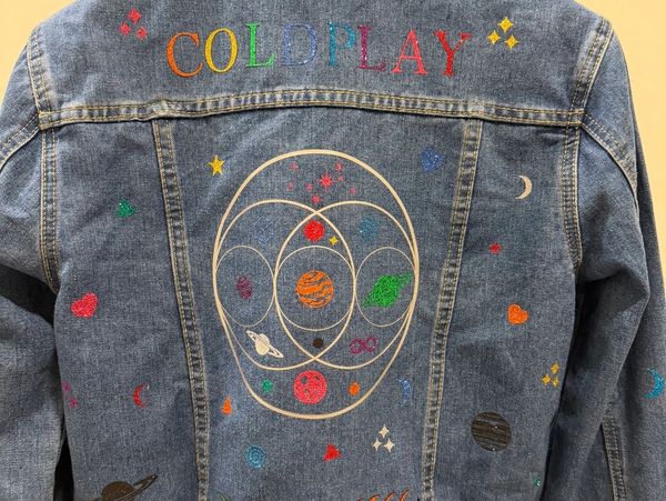 Denim jacket with colorful Coldplay and space designs.