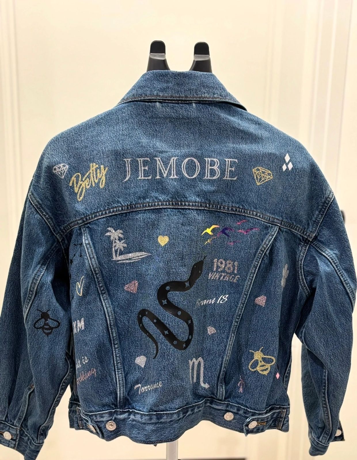 Denim jacket with colorful designs and text on the back.