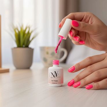 Hands applying bright pink gel nail polish indoors.