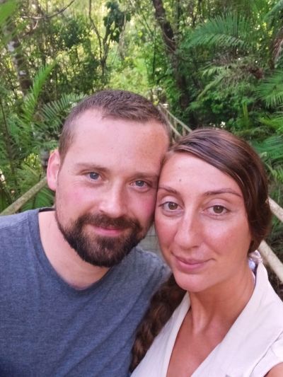 A couple taking a close-up selfie in a lush, green forest.