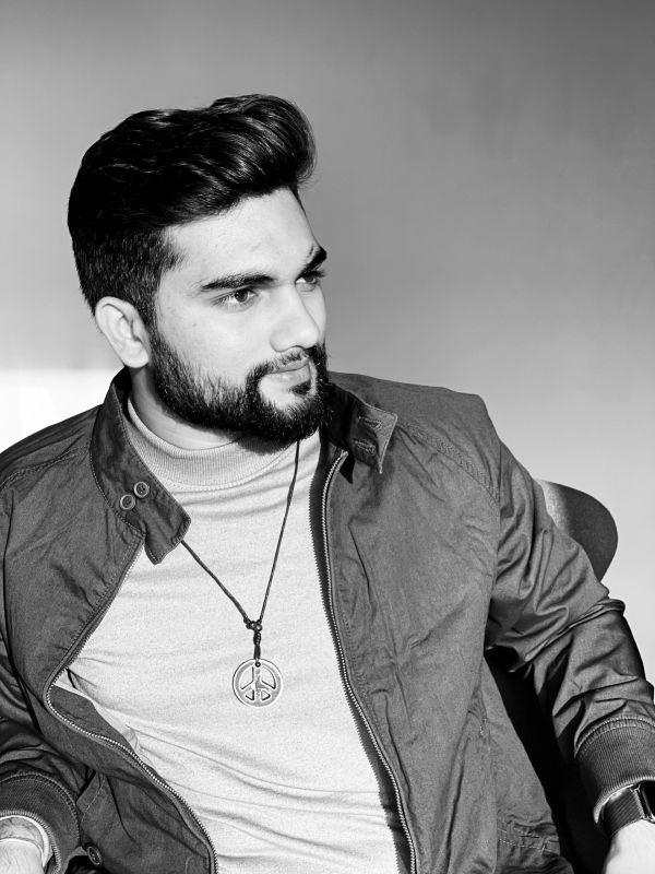 Black and white portrait of a man with a beard wearing a jacket and pendant.