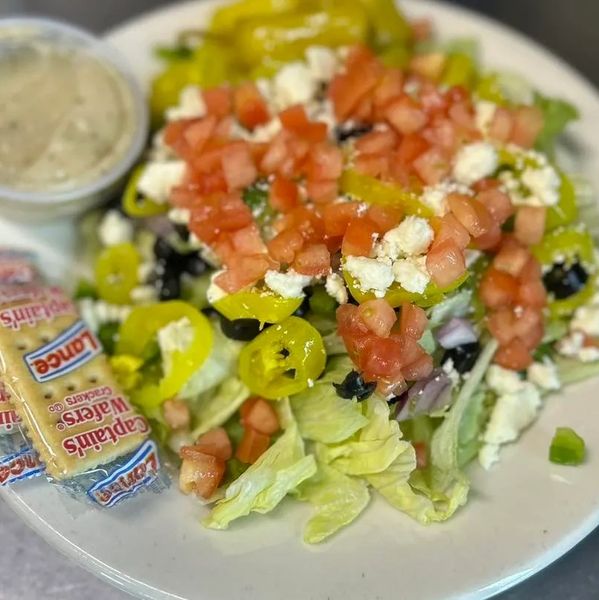 Fresh Greek salad with tomatoes, feta, olives, and pepperoncini, served with crackers and dressing.