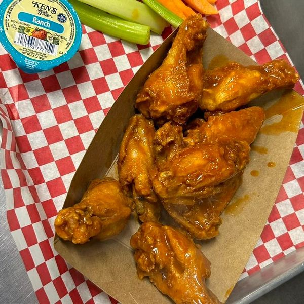 Buffalo wings served with celery, carrot sticks, and ranch dressing on a checkered paper.