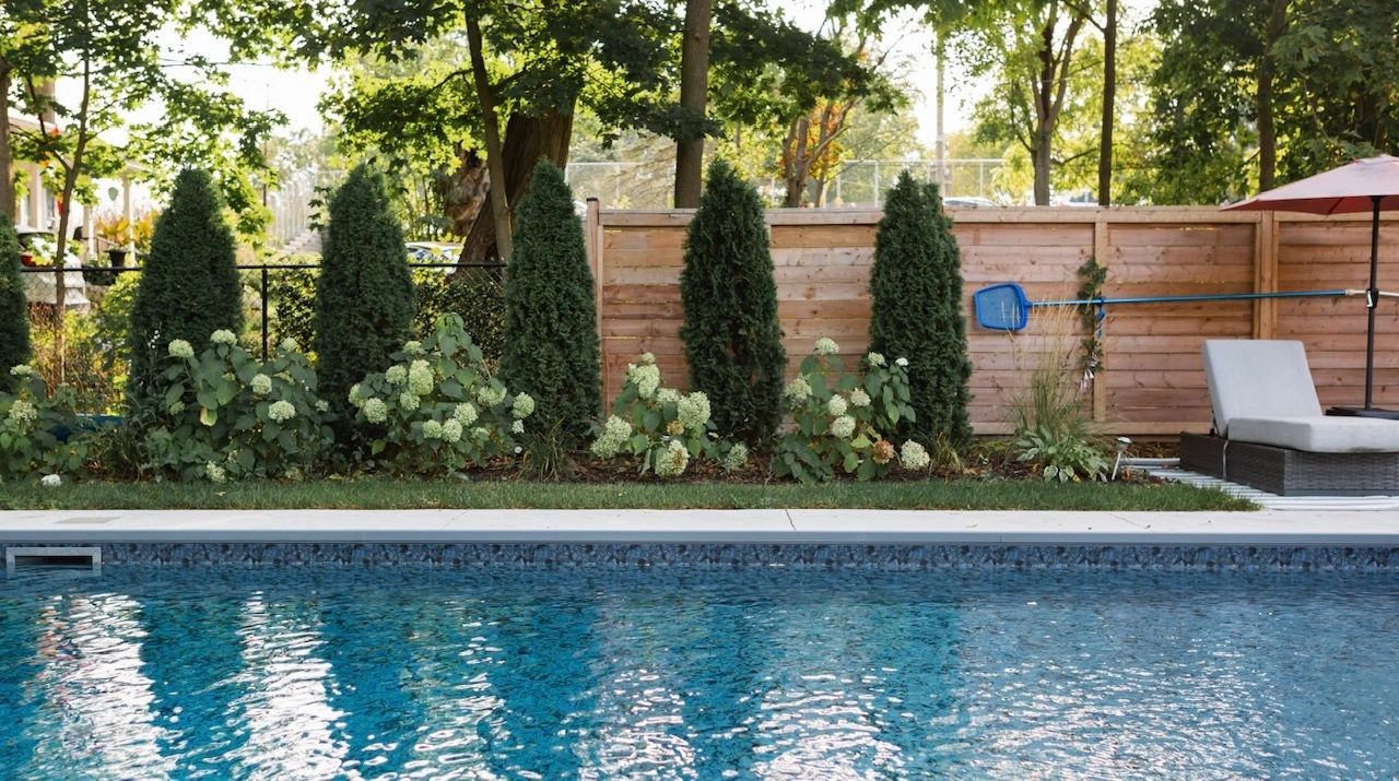 Lounge chairs and umbrella near a swimming pool, wooden barrel sauna in view.