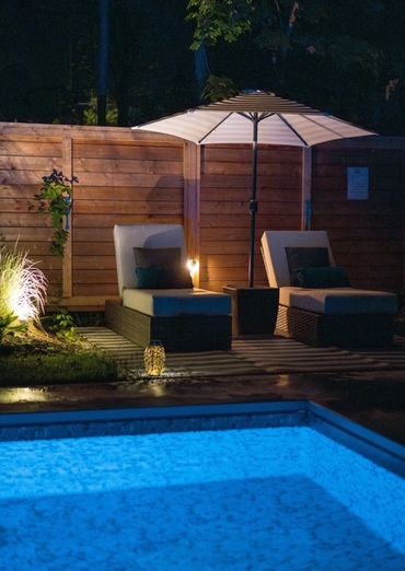 Swimming pool scene featuring two lounge chairs under an umbrella and a sauna.