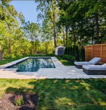 Wooden barrel sauna positioned next to a swimming pool and two lounge chairs.