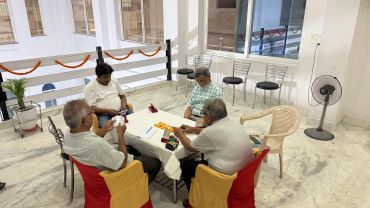 Four elderly men playing a board game indoors.