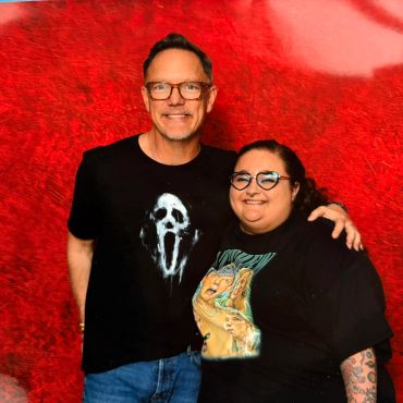 Two smiling people posing against a vibrant red backdrop.
