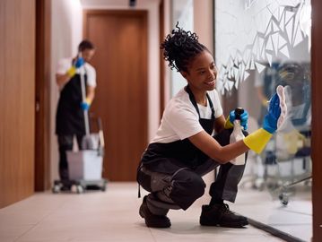 A woman cleaning a glass wall while a man mops the floor in a corridor.