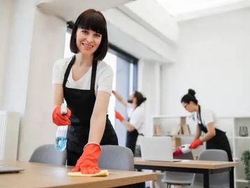 Woman cleaning a desk with two others working in the background.