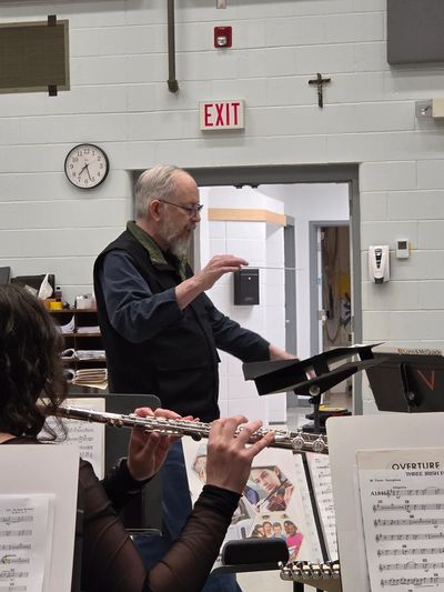 Man conducting a flute section in a music rehearsal room.