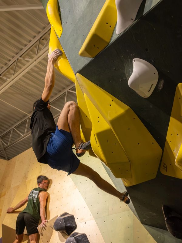 Two men indoor rock climbing on a wall with yellow and white holds.