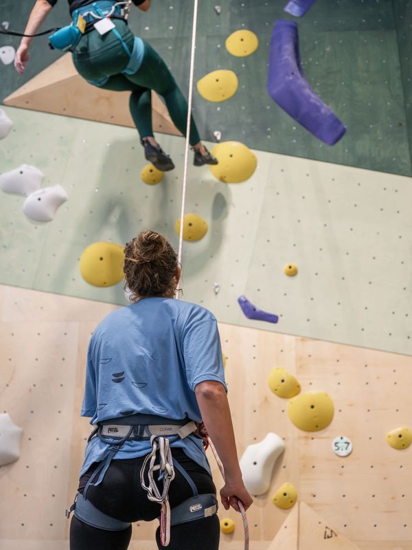 A person belaying another climber on an indoor climbing wall.