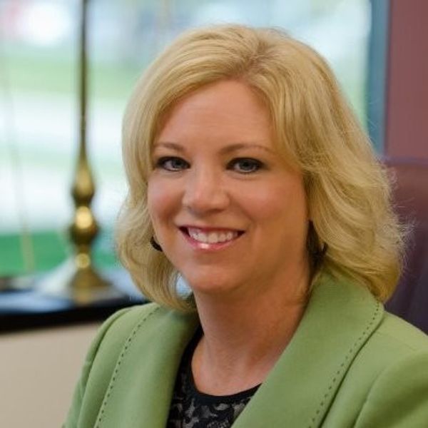 Smiling woman with blonde hair in a green blazer.