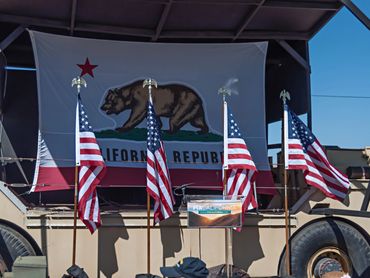 California Bear flag with 4 American Flages in front of it.