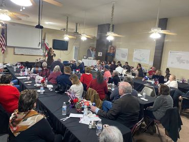 The dinner room is full of people with no seats available.  Guest speaker Jessie Jane Duff is speaki