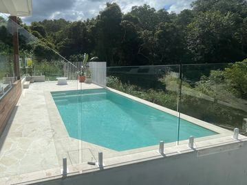 Modern swimming pool with glass fence and forest background.