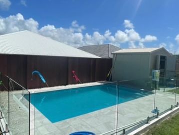 Outdoor swimming pool with glass fence and bright sky.