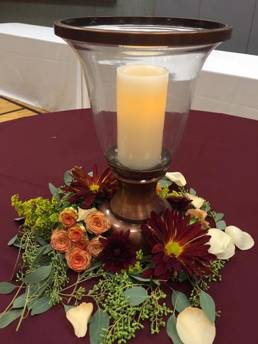 A centerpiece with candle and flowers with leaves