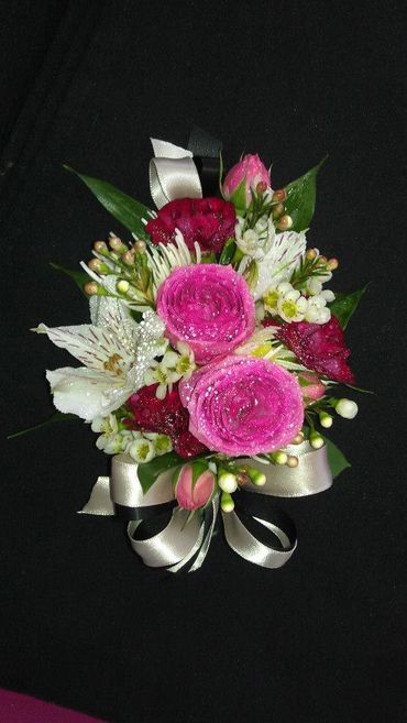 A hot pink and dark red corsage with a white ribbon