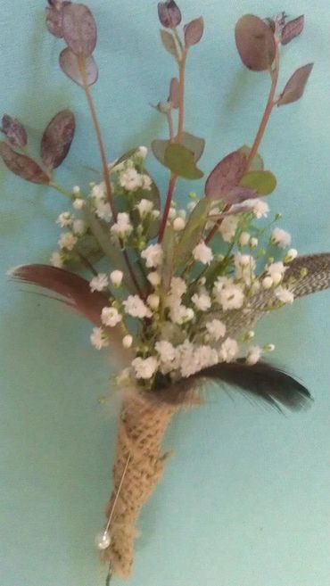 A pink boutonniere with small white flowers and feathers