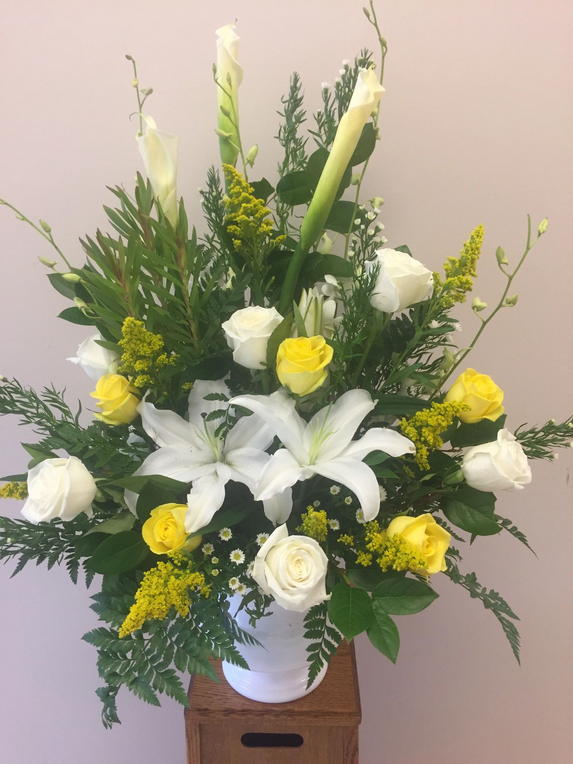 A white vase with yellow and white sympathy flowers