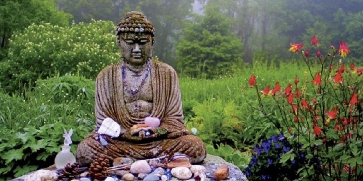 Buddha statue surrounded by nature and offerings in a serene garden.