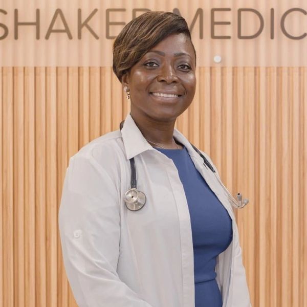 RN Jodie Wilson, FNP -C, wearing a white coat stands in front of a Shaker Medical Group sign.