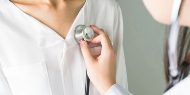 Close up of a Doctor holding a stethoscope to the chest of a female patient.