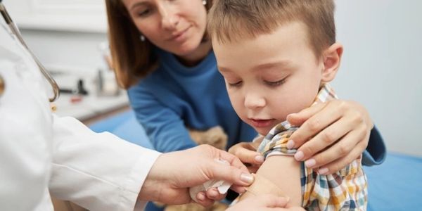 Doctor placing medical plaster on child arm after vaccination.