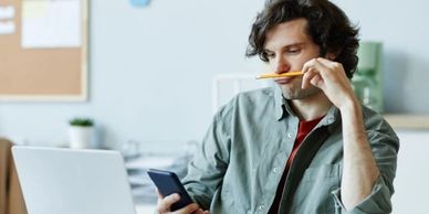 Portrait of a Caucasian young man playing with pencil and using phone at work suffering from ADHD.