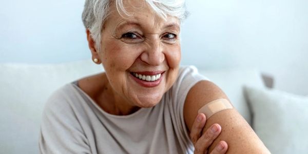 Proud mature woman smile after vaccination with bandage on arm.