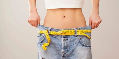 Female with a flat stomach holds loose fitting jeans by the side as they practically fall off.