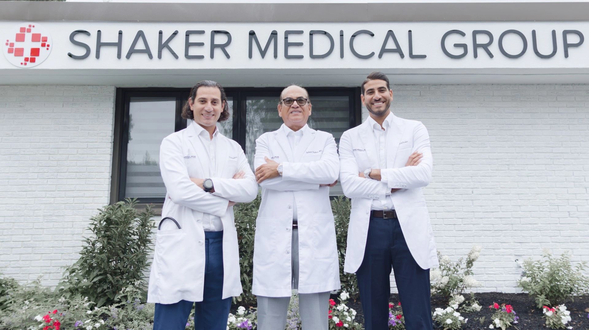 Three doctors wearing white lab coats stand in front of the building for Shaker Medical Group.