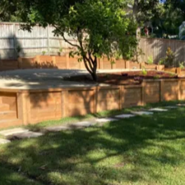 Sunlit backyard with wooden retaining walls and a tree.