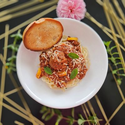 Spaghetti with meatballs, tomato sauce, and a toasted bun on top.
