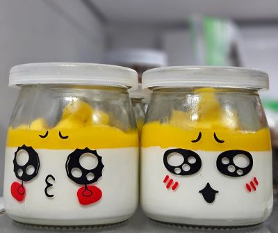 Two jars with cute faces and yellow cream on top.