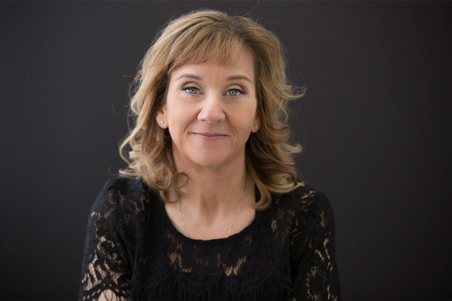 Confident woman with arms crossed, smiling slightly against a modern glass background.