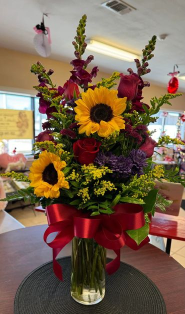3 Sunflowers,1/2 Red Roses, Maroon Snap Dragons, Purple and Maroon Poms, Yellow Solidago in Standar