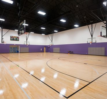 Spacious high school gymnasium with polished wood flooring, basketball hoops, purple accent walls.