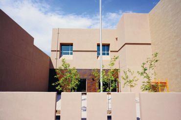 Courtyard view of a two-story school building with stucco walls and young trees.