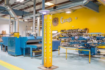 Screen printing area at Deluxe Design with bold yellow walls and industrial equipment.
