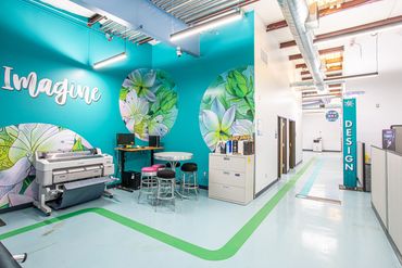 Creative design studio at Deluxe Design with teal accent wall and floral graphics.