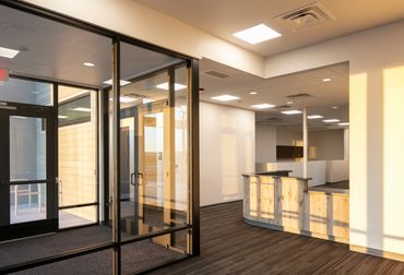 Modern office interior with glass entry, natural light, warm finishes reflecting minimalist design.