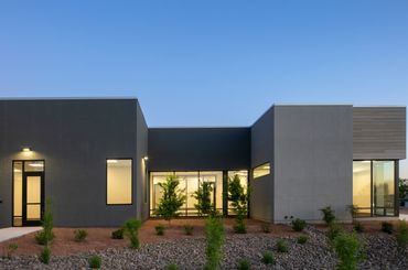 Modern office building with geometric façade, large windows, and desert landscaping at twilight.