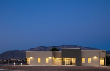 Modern single-story office building illuminated at dusk with mountain backdrop and clean geometric d