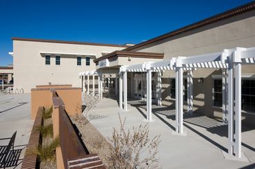 Exterior walkway with white pergola structure and modern stucco façade under clear blue sky.